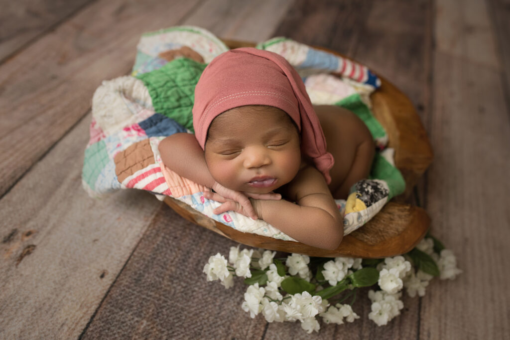 newborn baby girl on colored quilt laying in bowl surrounded by white flowers