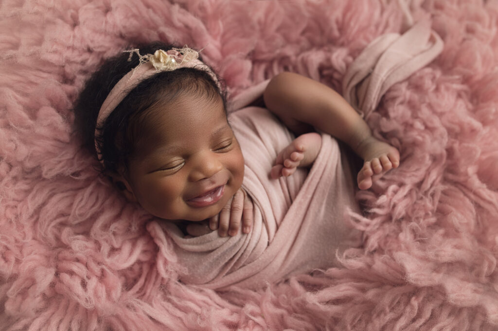 Newborn Baby Girl in pink fur with matching pink wrap and bow