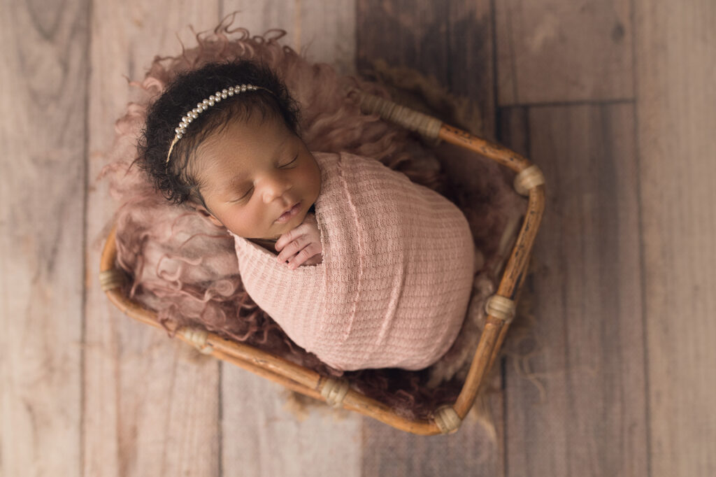 Newborn Baby Girl in Pink Wrap laying in a bamboo basket