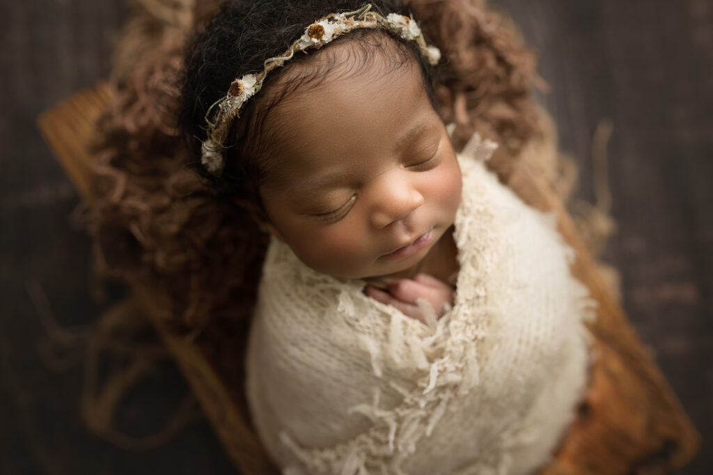Newborn Baby Girl with flower crown laying in brown trench bowl in cream wrap