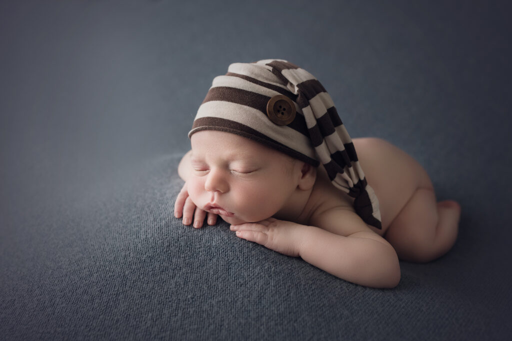 newborn baby boy face forward on blue blanket with brown striped sleepy cap