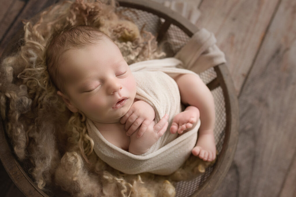 newborn baby boy wrapped in beige wrap in wooden bowl