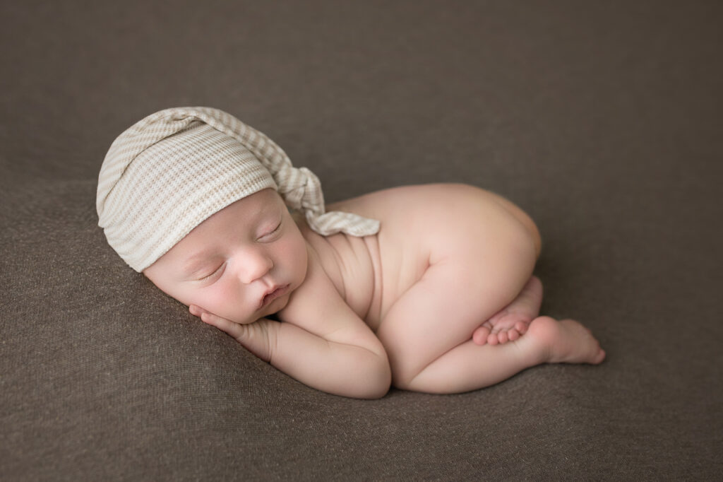 newborn baby boy with bum up on a brown blanket with striped sleeper cap