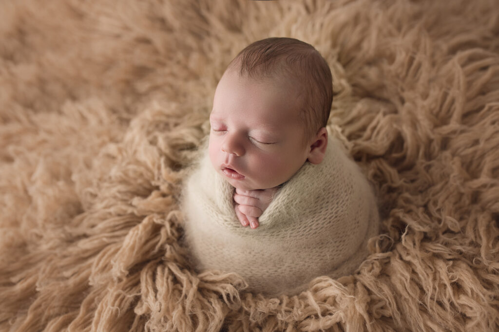 Newborn baby boy in beige fur wraped in beige