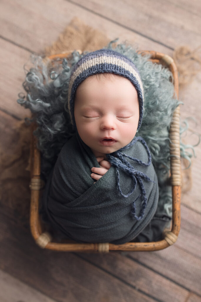 Newborn baby boy in basket wrapped in a blue wrap with matching hat