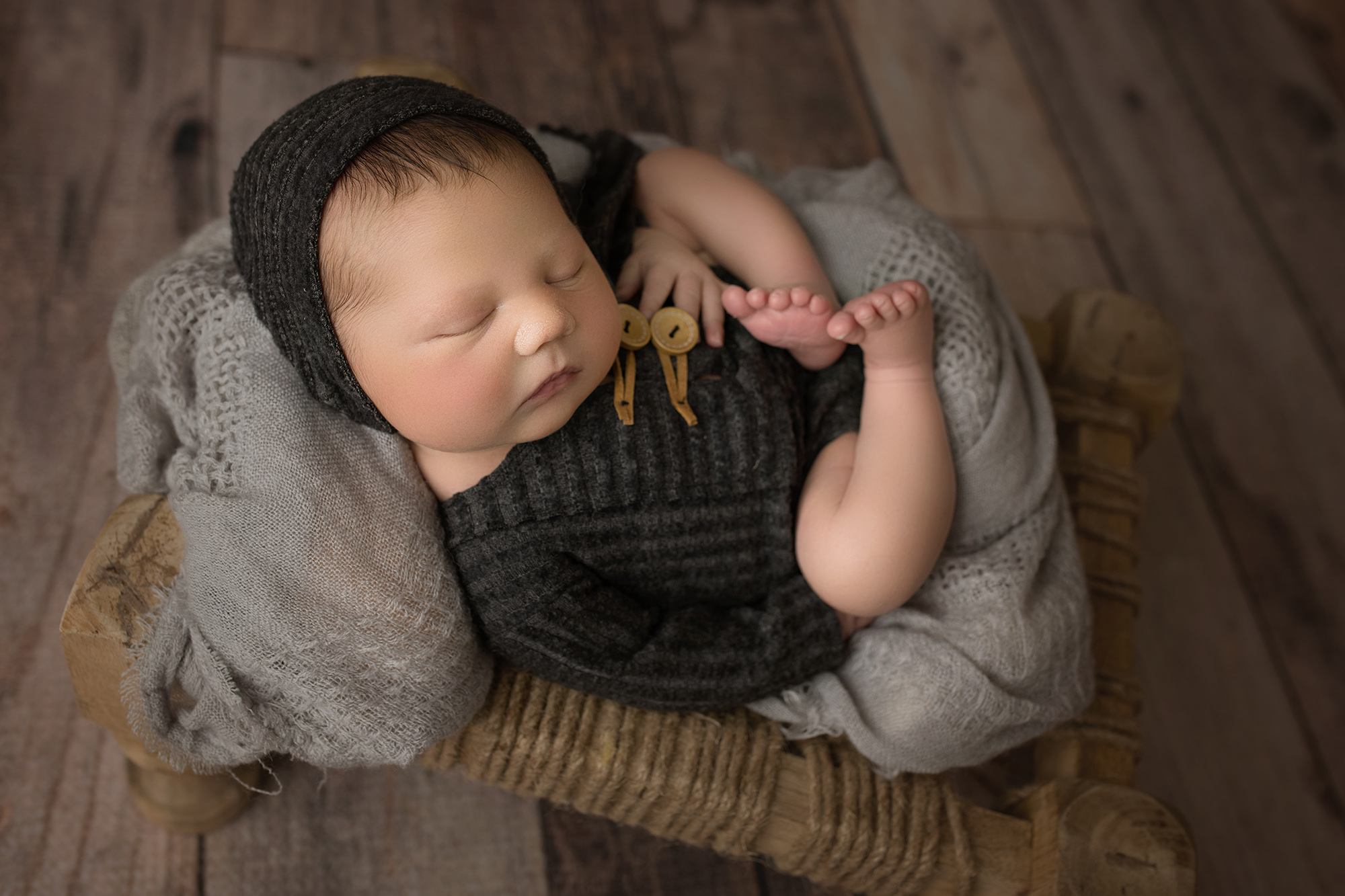 newborn baby boy with gray outfit and matching bonnet laying face up on stool