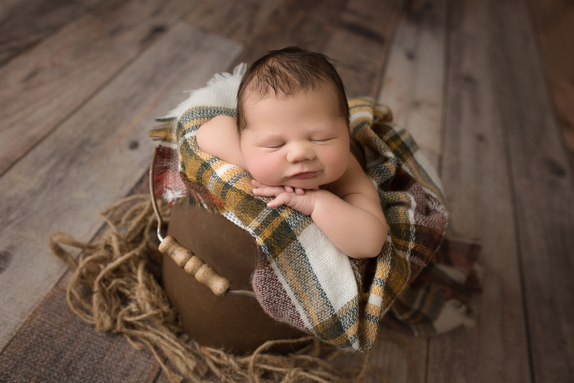 Newborn baby boy in brown bucket and plaid blanket