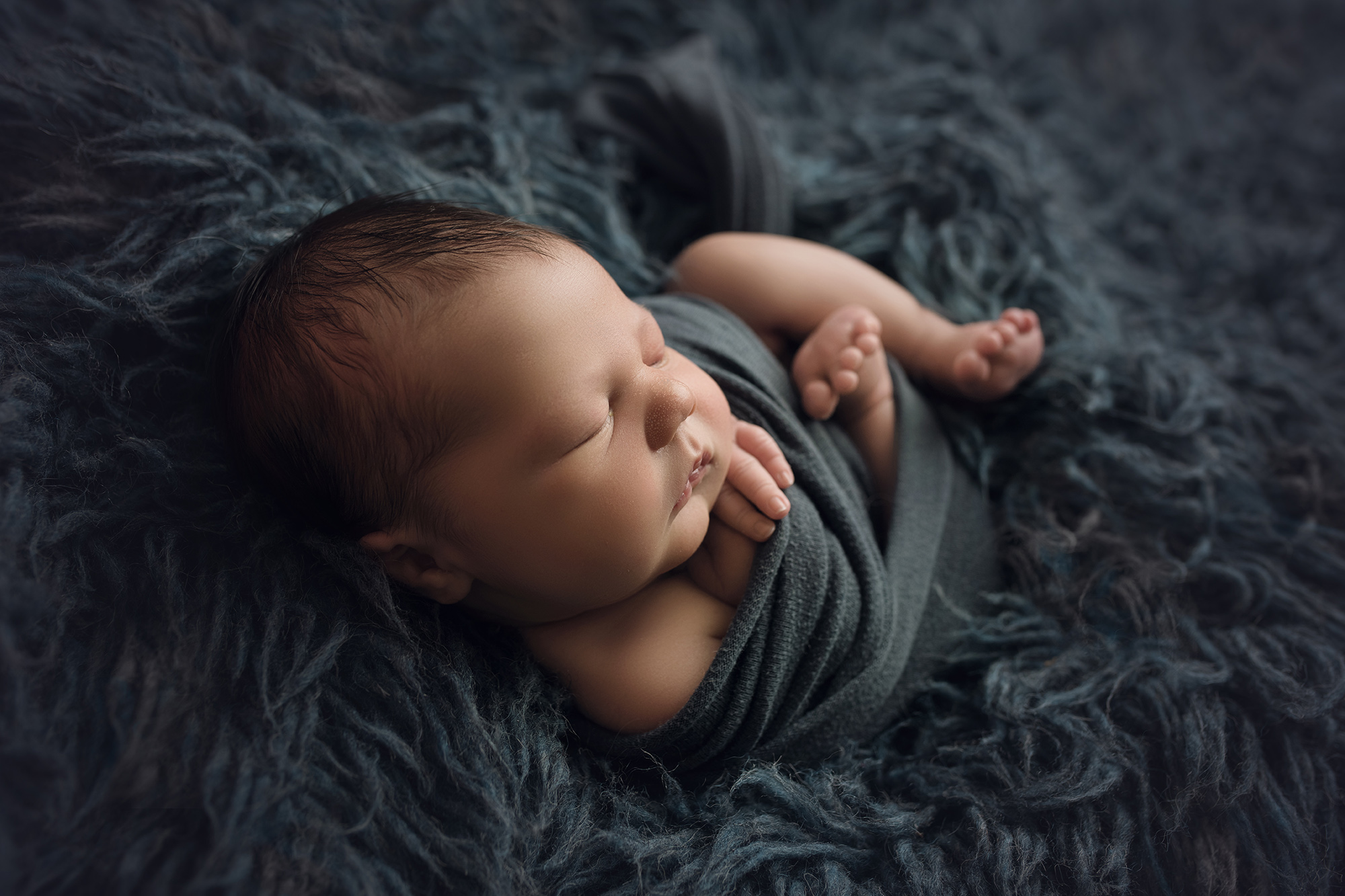 newborn baby boy on blue fur wrapped in blue