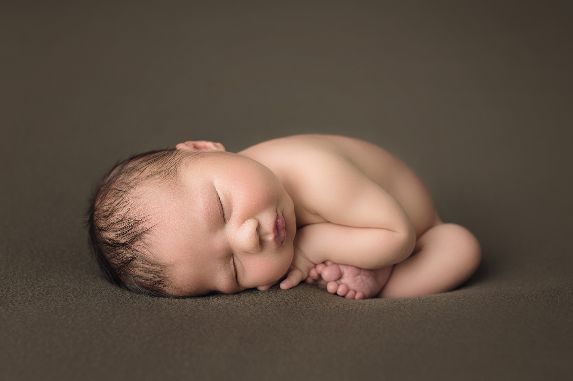 newborn baby boy in womb pose on green blanket