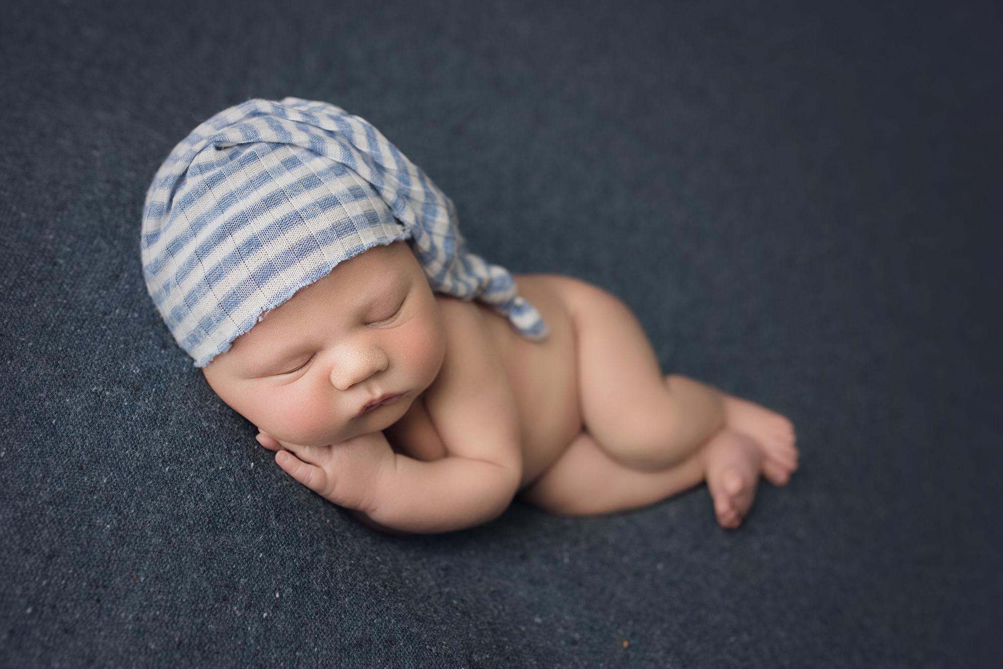 newborn baby boy side sleeping in striped blue sleepy hat on blue blanket