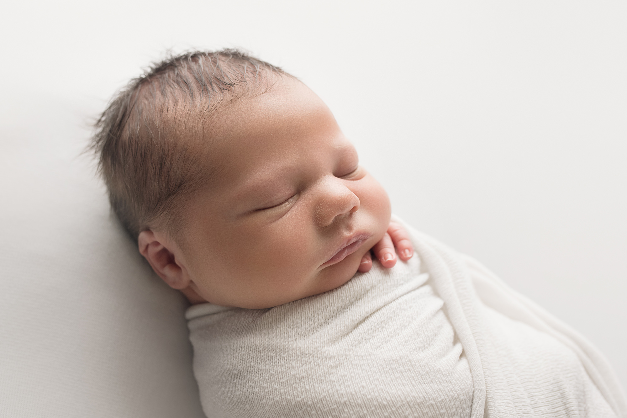 newborn baby boy in white wrap backlit