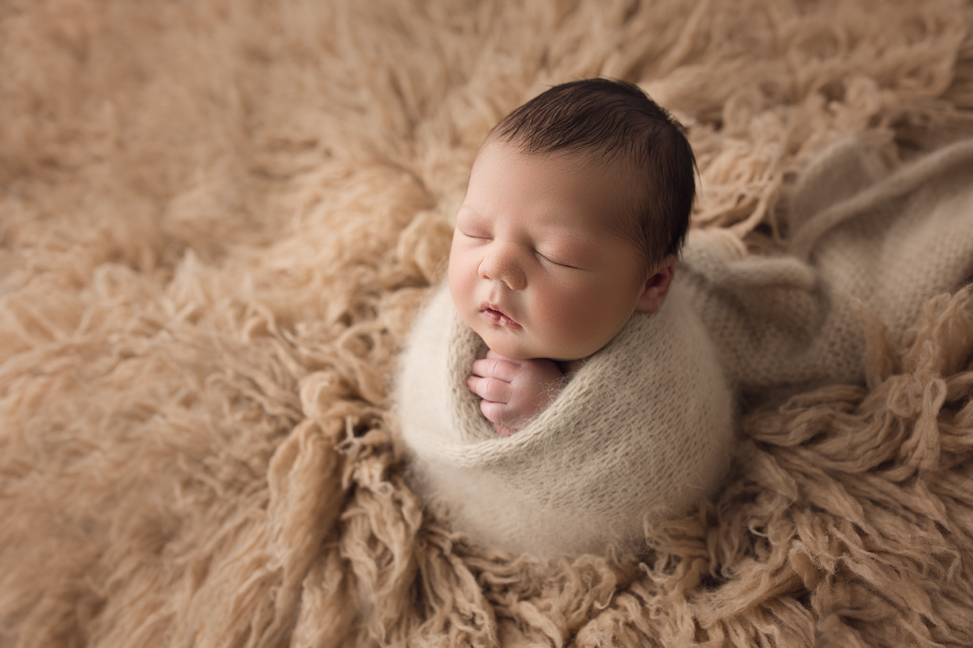 newborn baby boy in beige wrap on beige fur