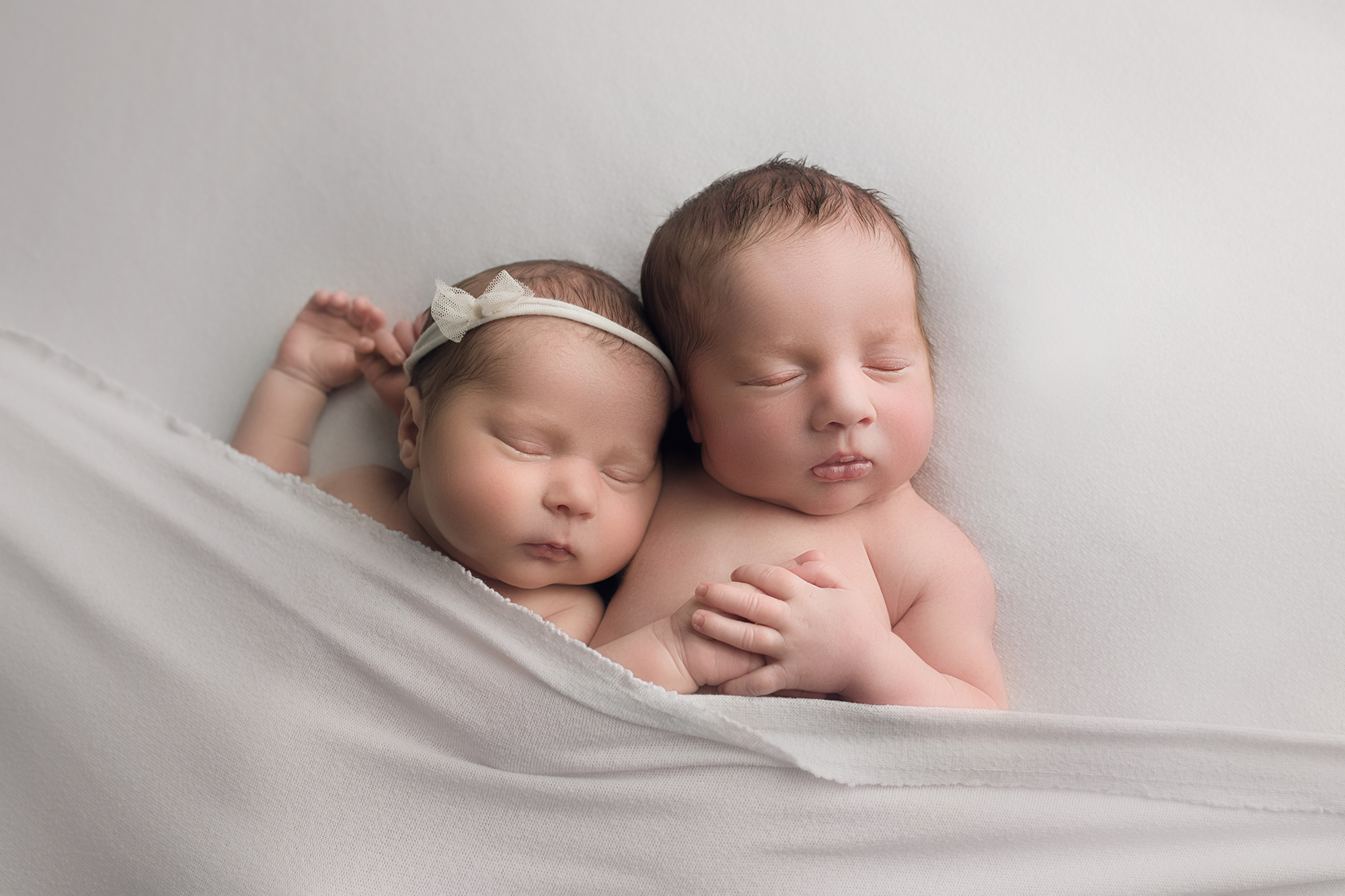 Newborn twins laying on white blanket cuddling
