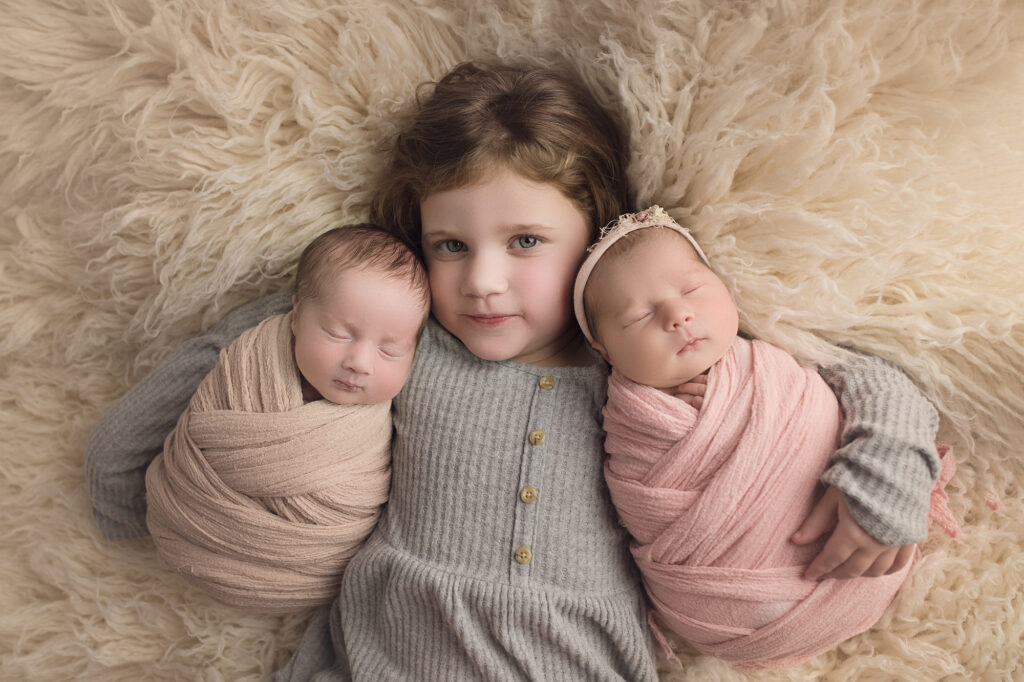 Newborn twins wrapped with big sister