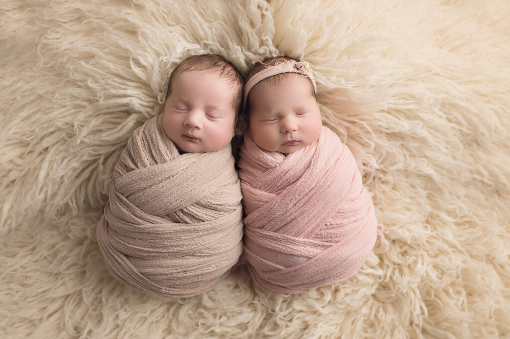 newborn twins wrapped in pink and beige on white fur