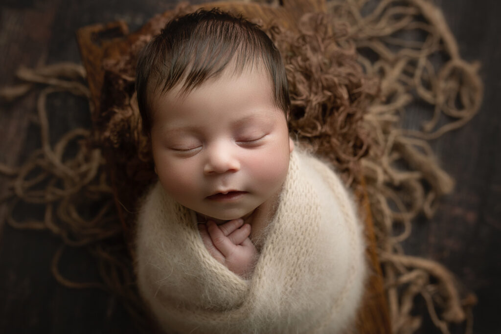 newborn baby boy wrapped in tan fuzzy wrap in bowl