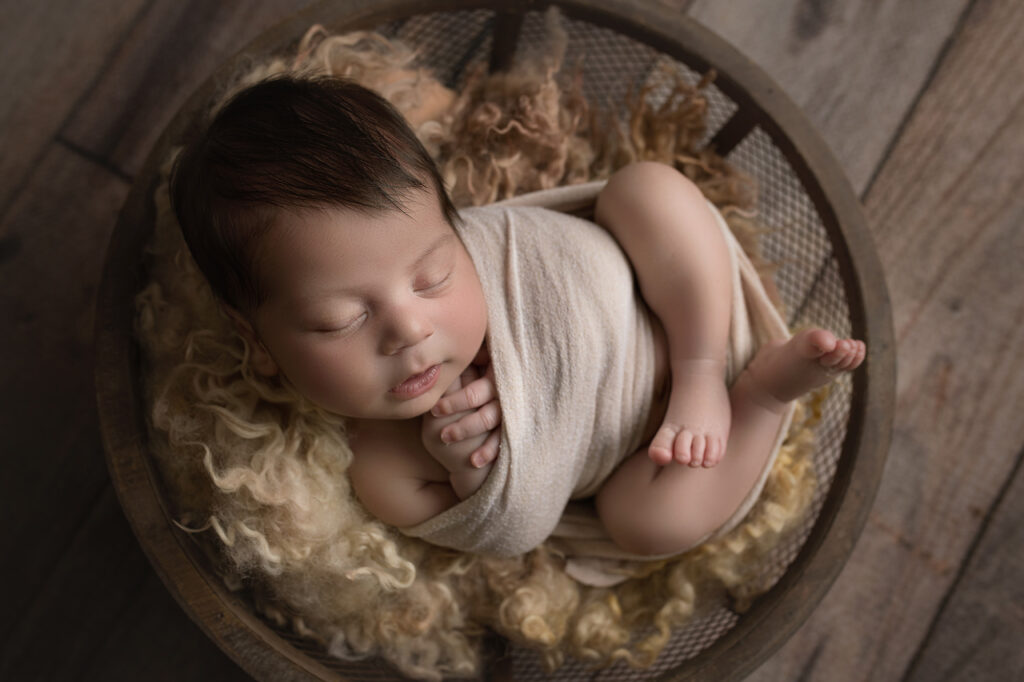 newborn baby boy wrapped in beige wrap in wire bowl