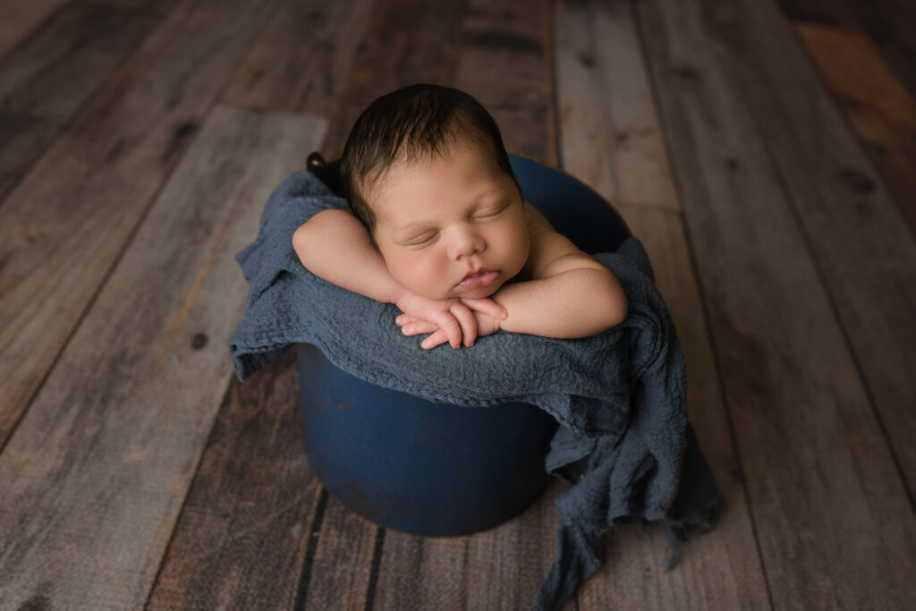 newborn baby boy in blue bucket facing forward on blue wrap