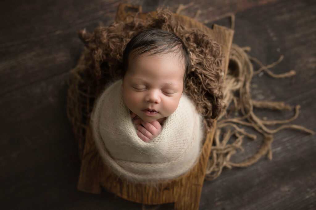 newborn baby boy in fuzzy wrap in brown wooden bowl