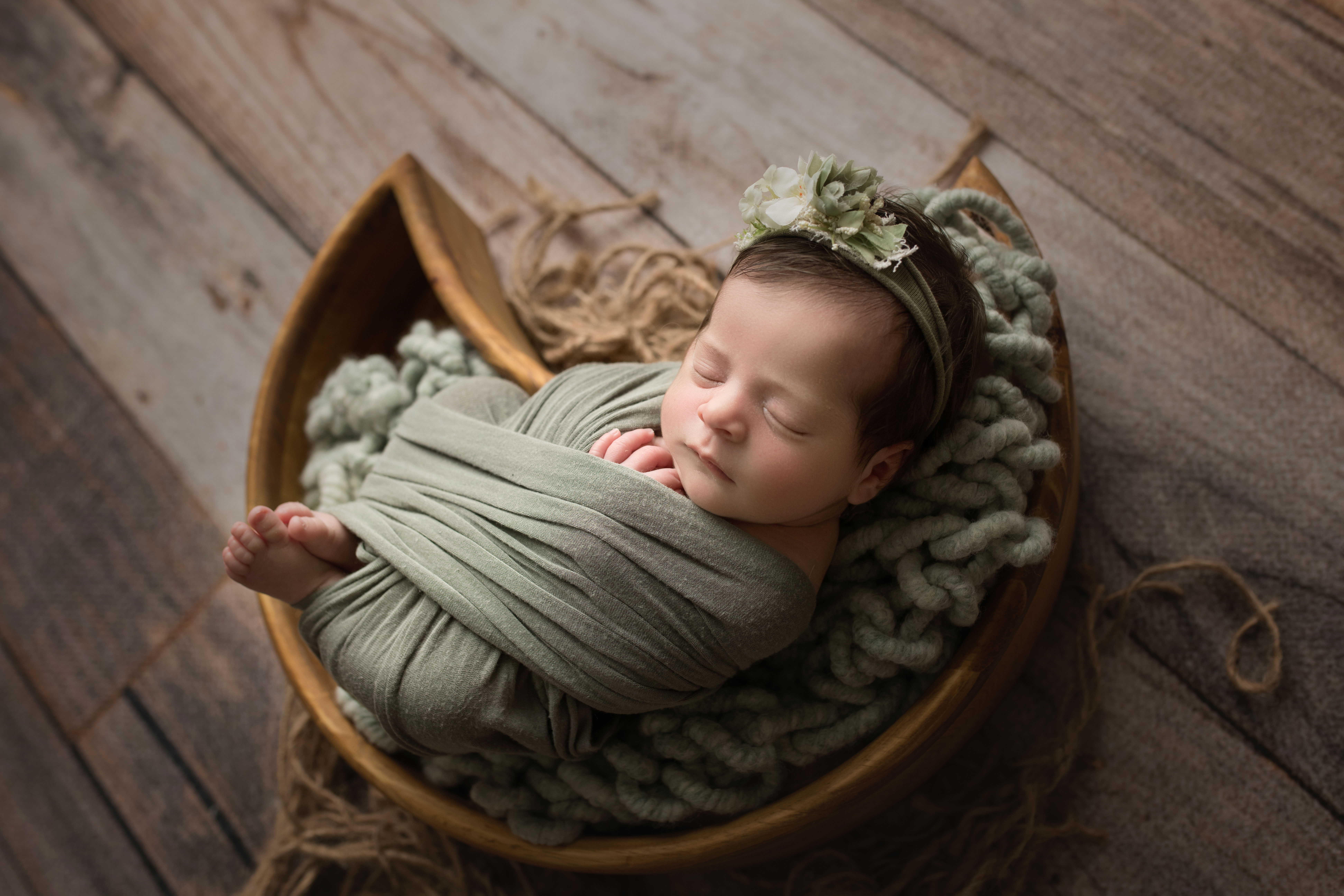 newborn baby girl laying in wooden moon prop in green wrap
