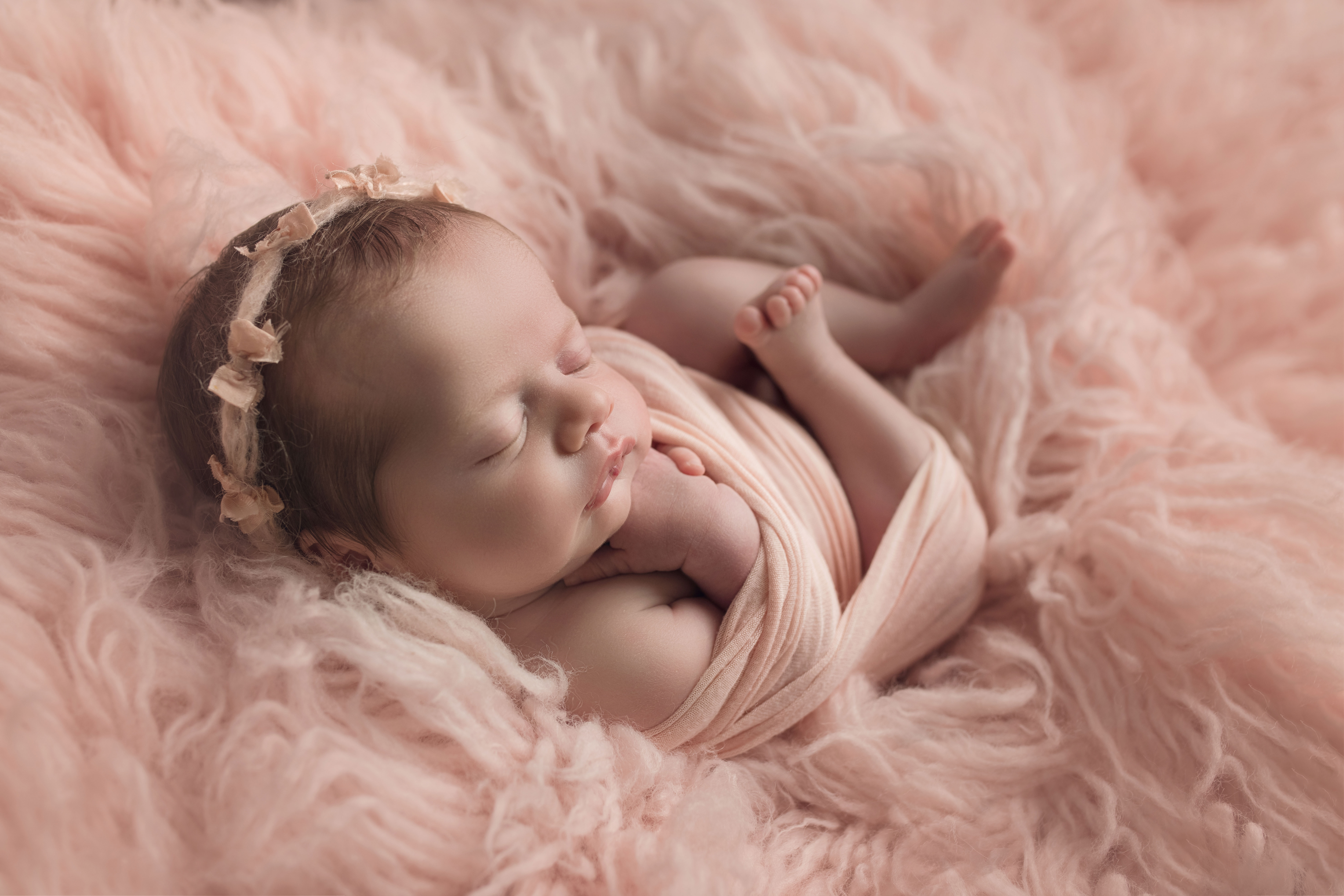 newborn baby girl in pale pink fur in pink wrap
