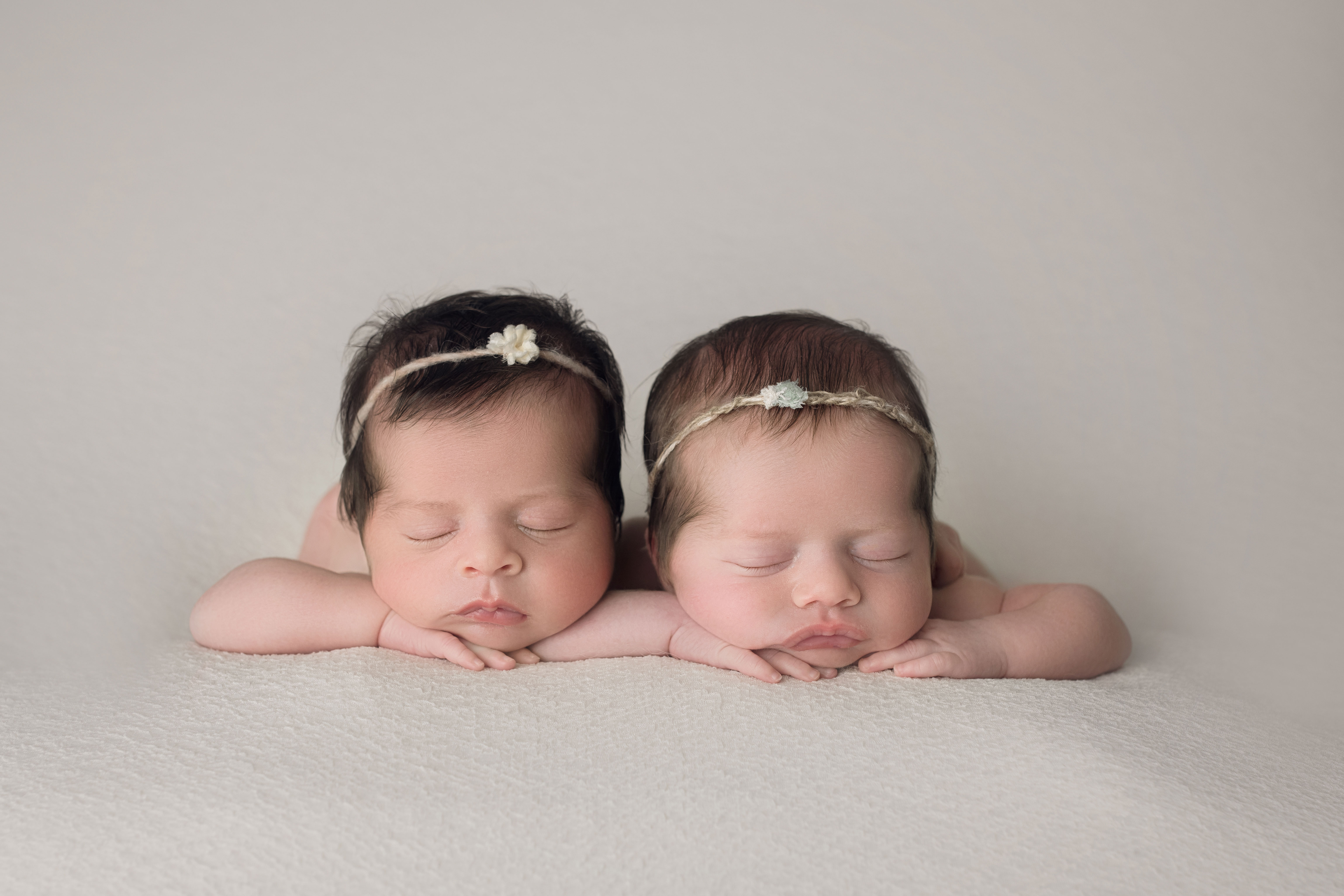 newborn twin girls face forward on white wrap