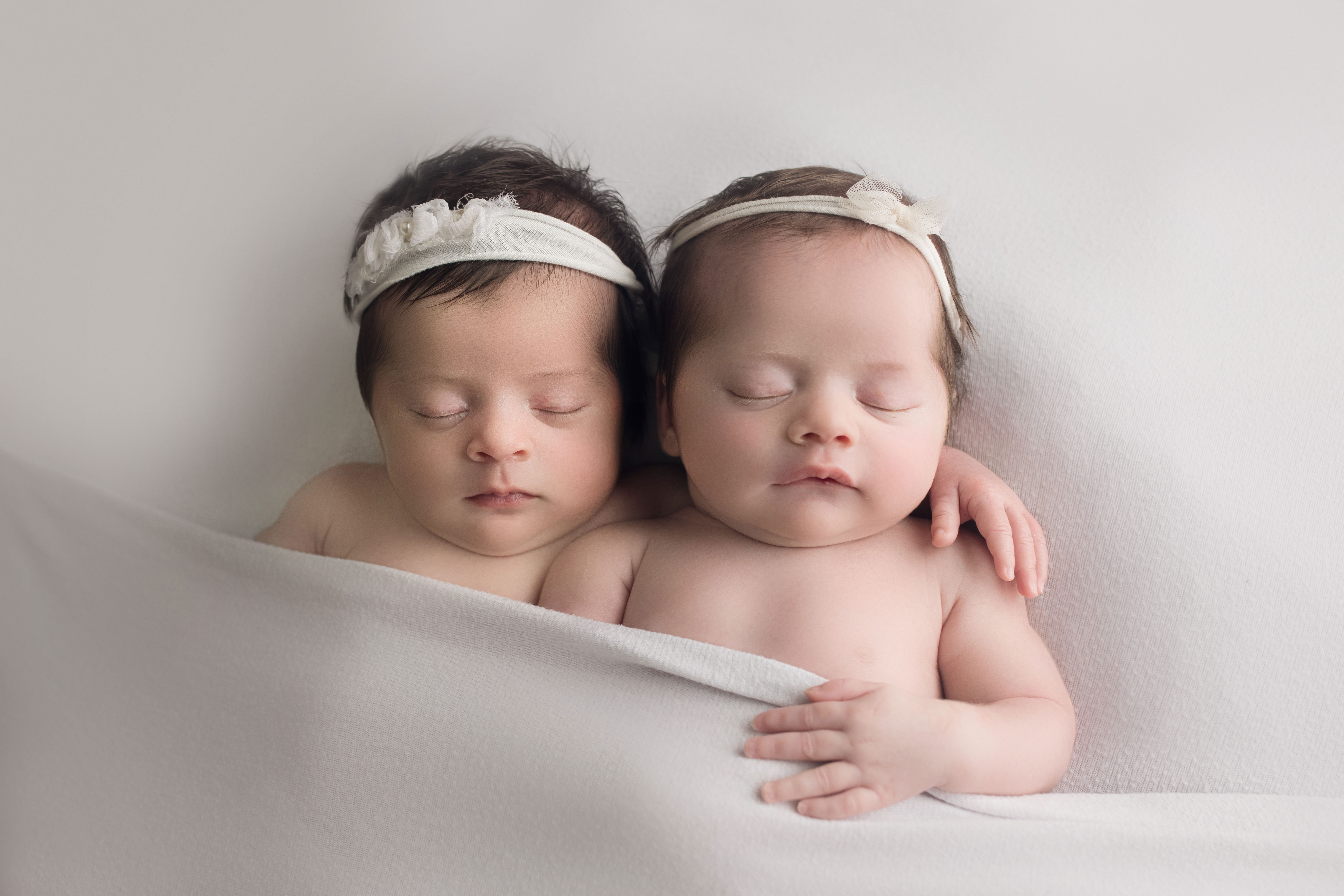 newborn twin girls laying side by side on white
