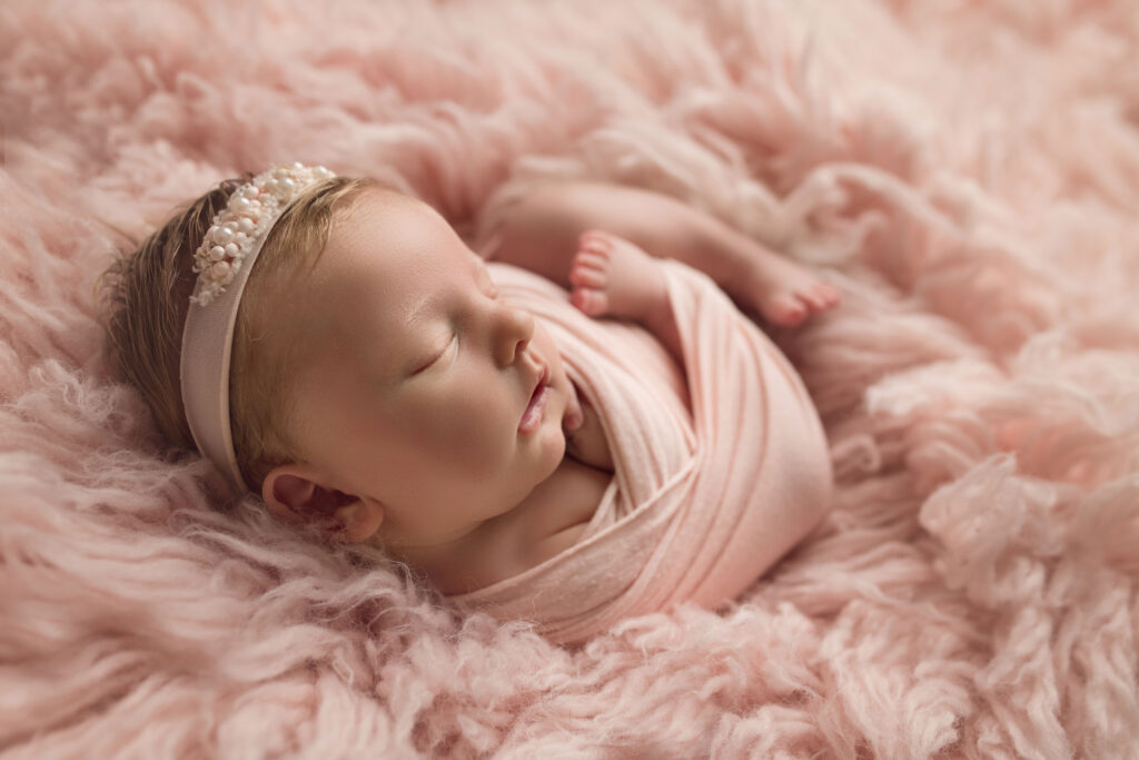 Newborn Baby Girl wrapped in pink laying on pink fur