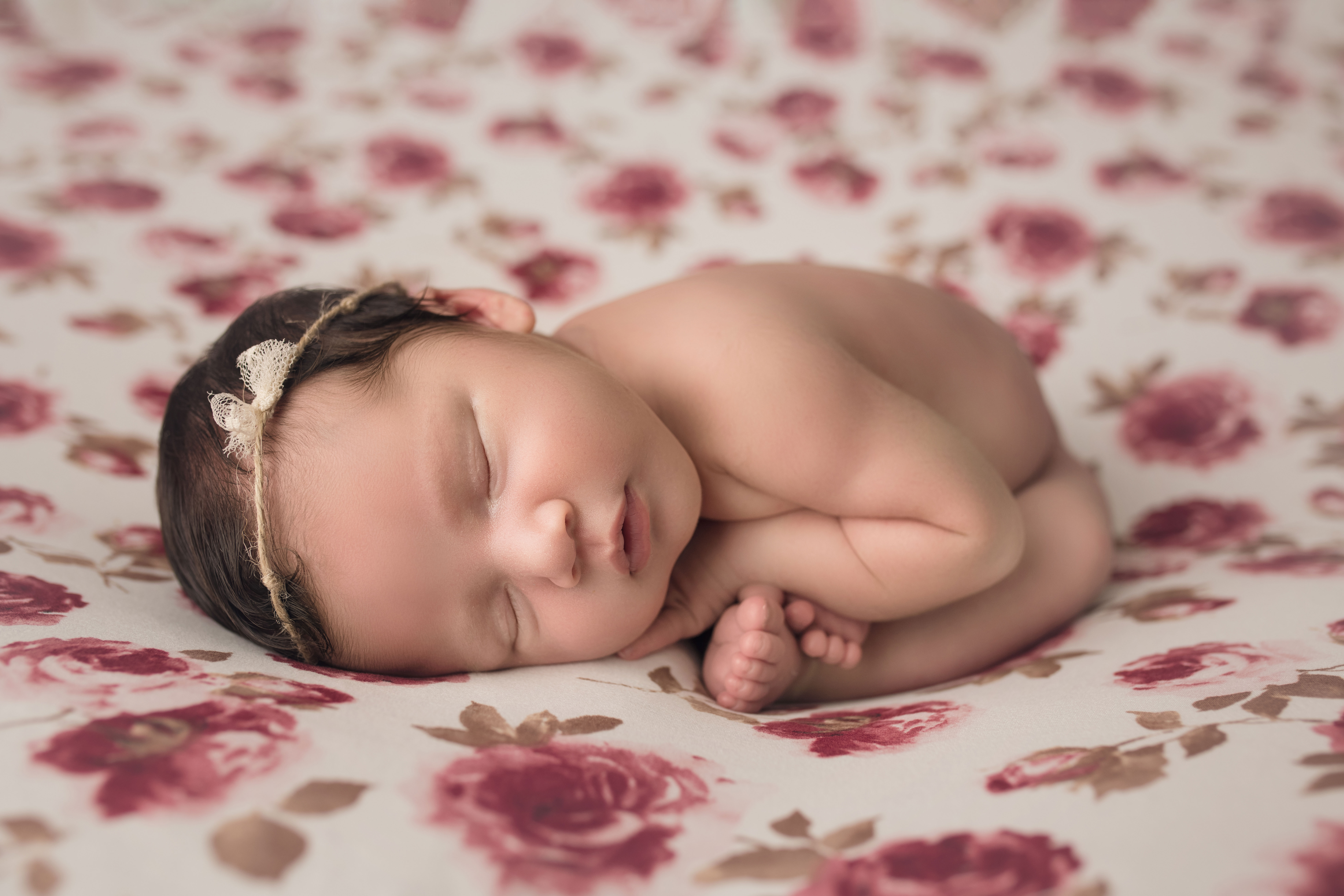 Newborn baby girl in womb pose on floral blanket