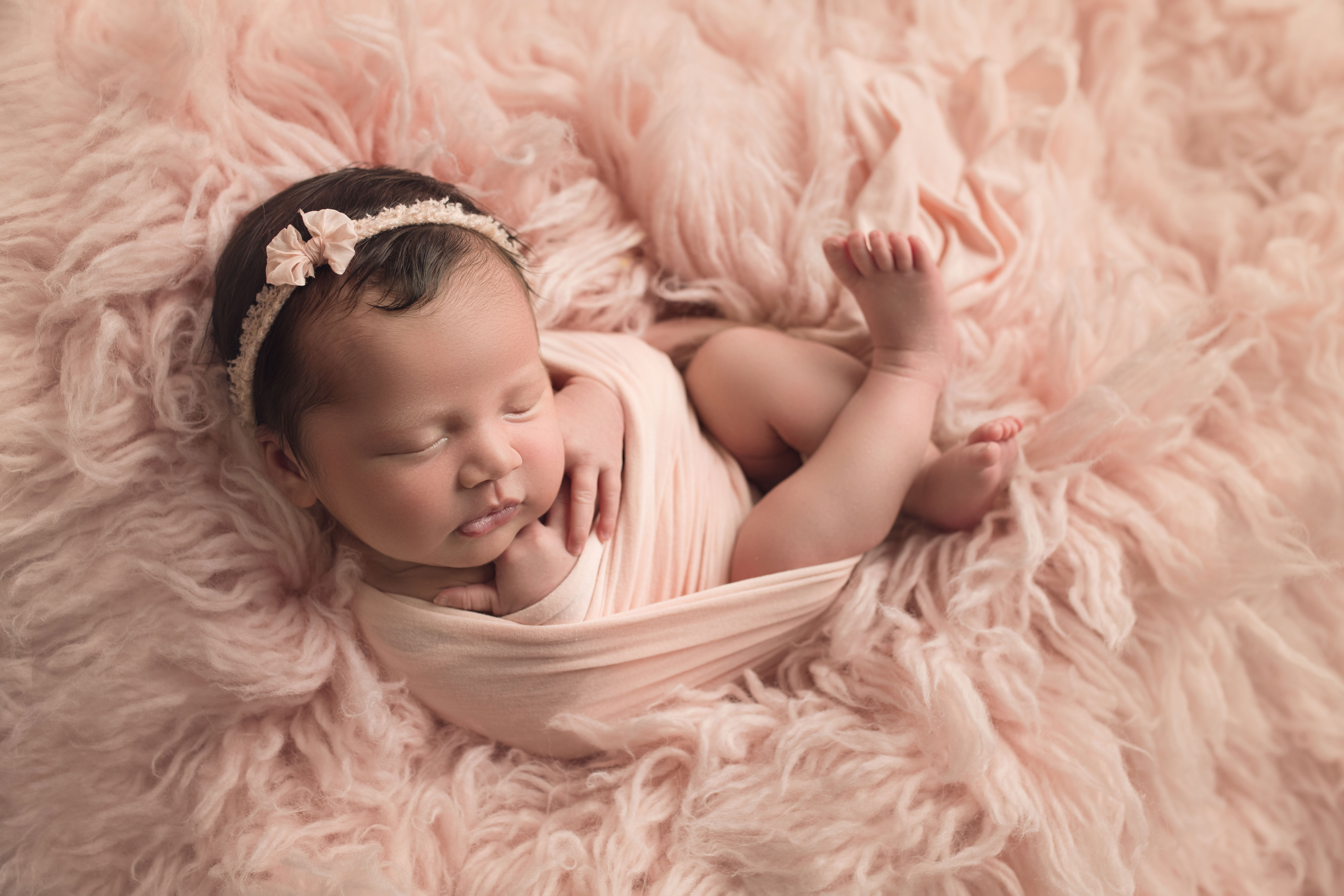 newborn baby girl in pink fur with pink wrap and headband