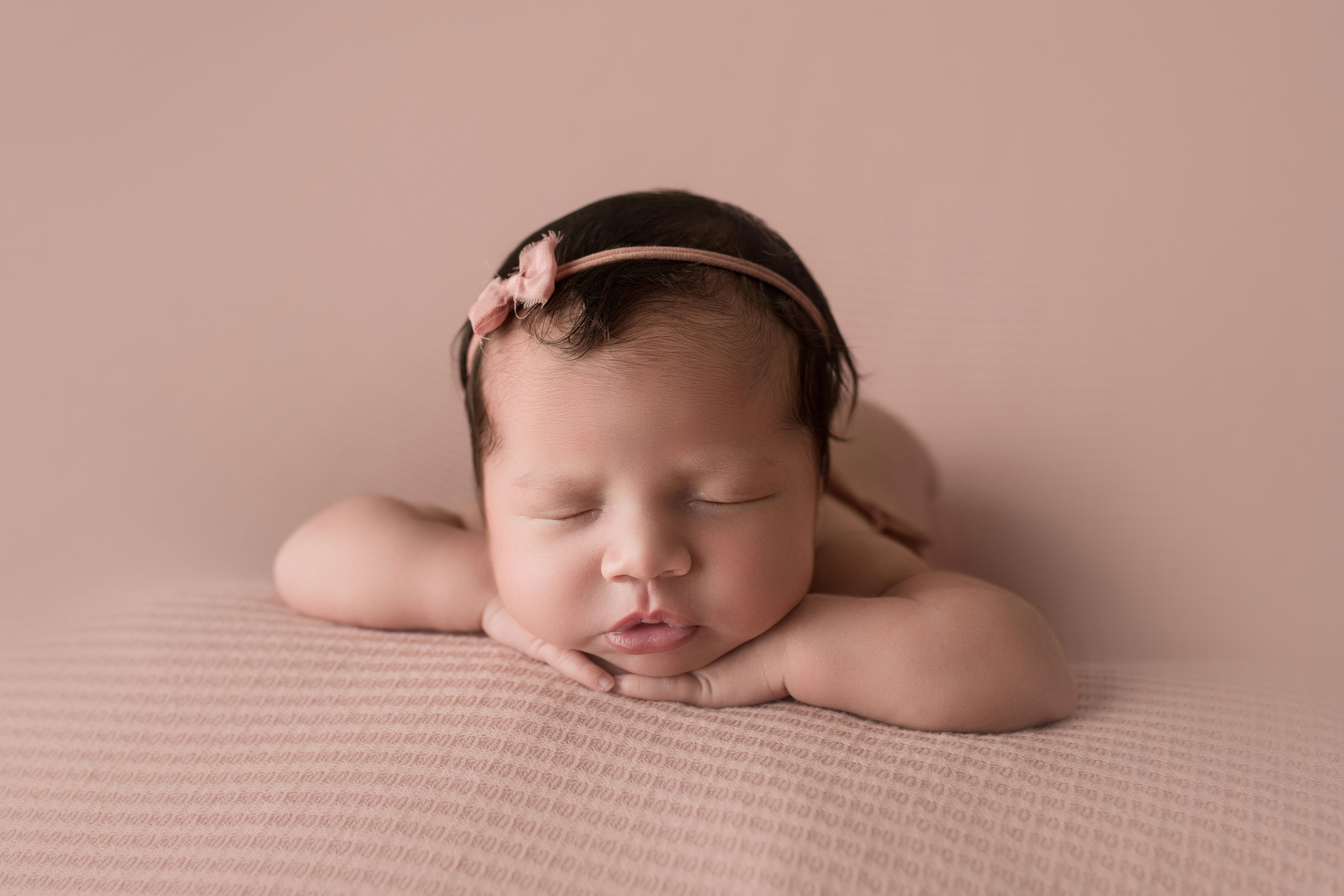 newborn baby girl face forward on pink waffle blanket