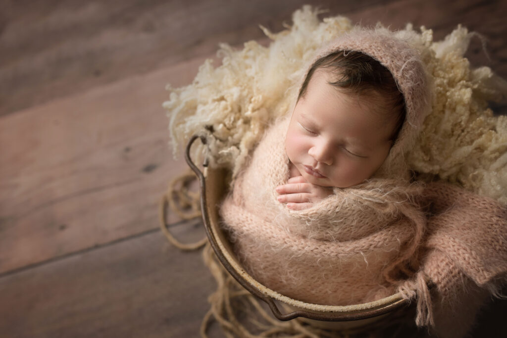 newborn baby girl wrapped in fuzzy pink wrap and hat in bucket Raleigh newborn baby photographer