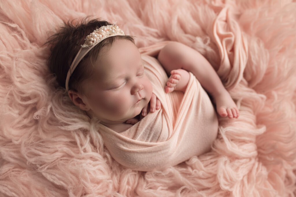 newborn baby girl sleeping in pink wrap curled into a pink flokati fur