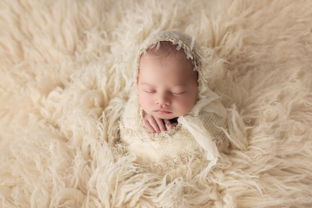 Newborn Baby Girl bum up laying on cream lace### Newborn Baby Girl in potato sack pose with cream frilly bonnet on white fur