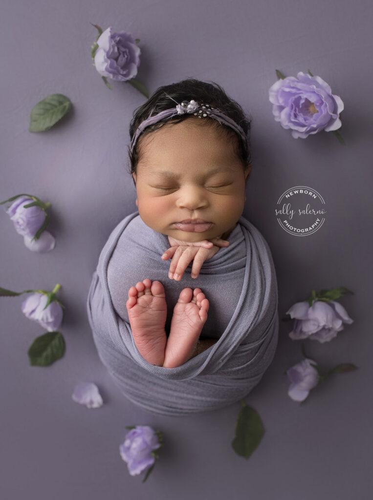 Newborn Baby Girl with purple flowers and purple blanket with toes sticking out