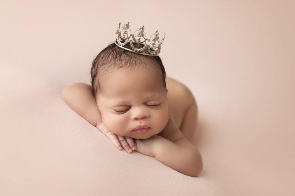 Newborn Baby Girl face forward on blush colored backdrop wearing a princess crown
