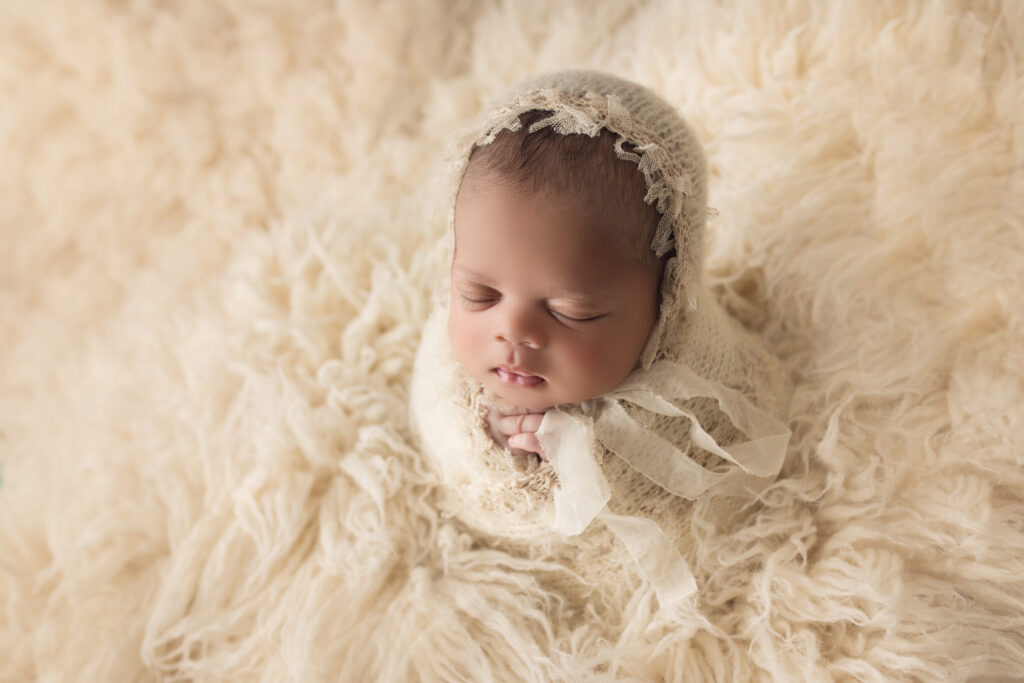 Newborn Baby Girl wrapped in a cream lace wrap with matching bonnet in potato sack pose