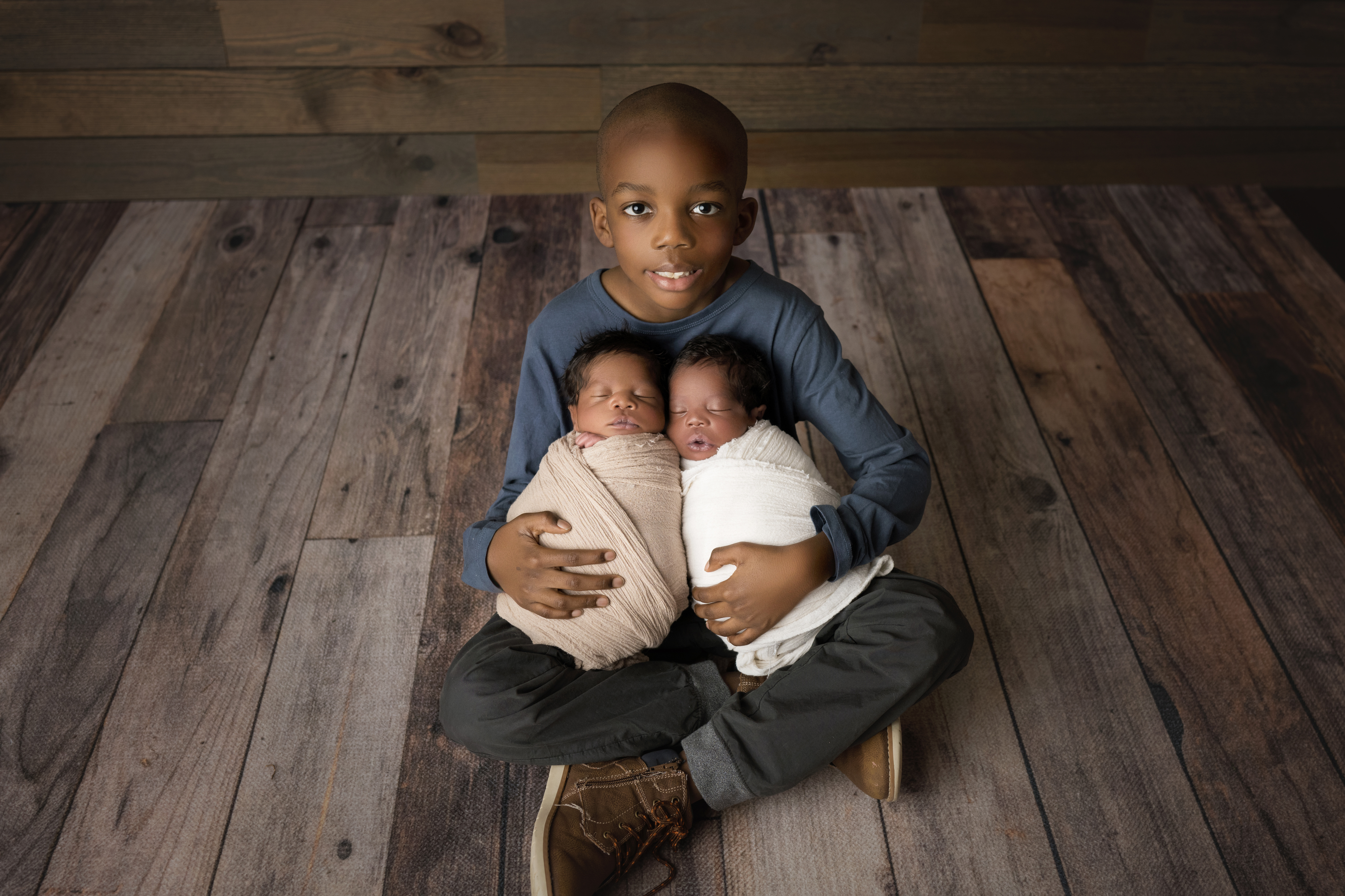 Newborn twin boys and big brother wrapped together snuggling