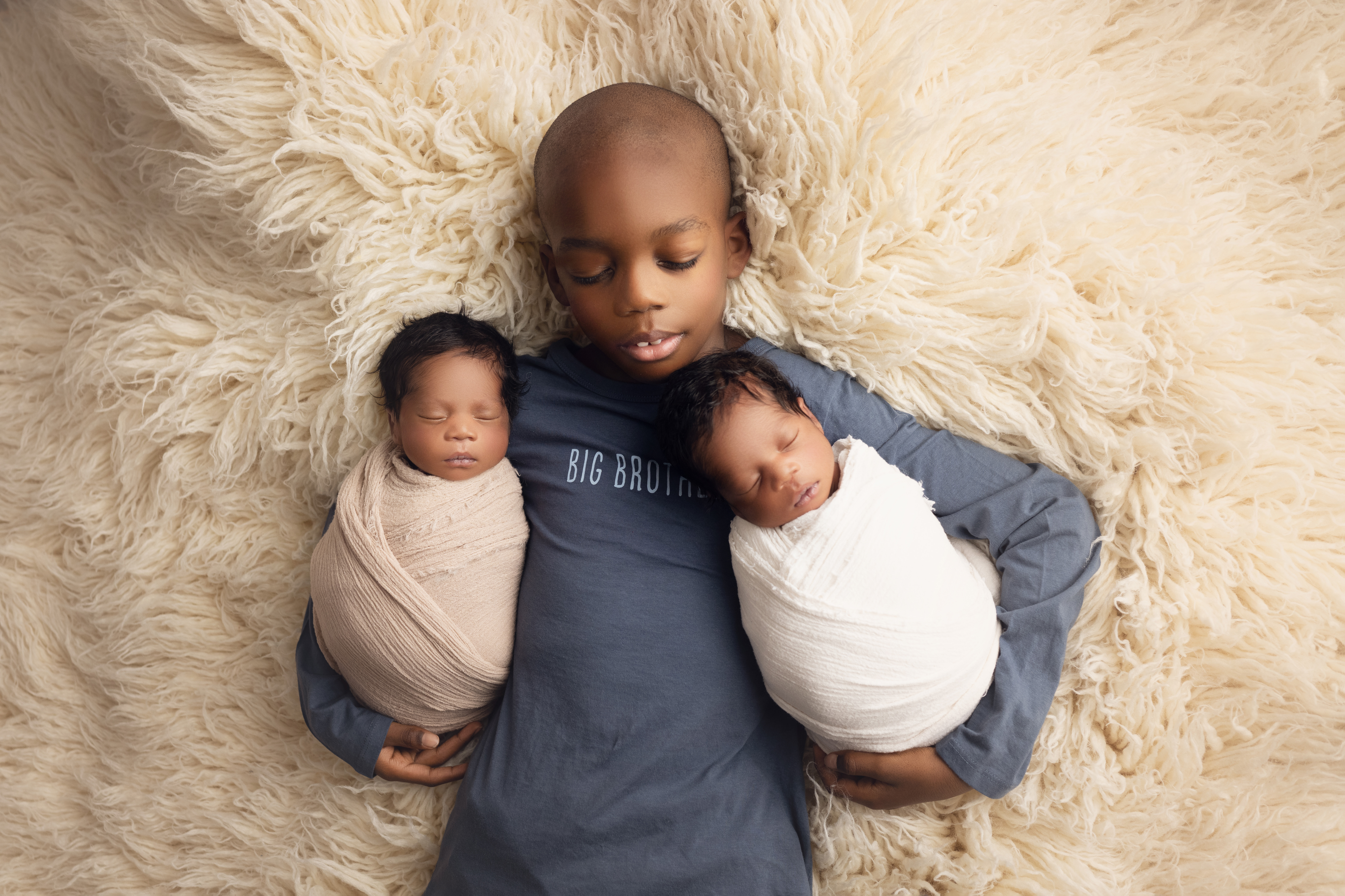 Newborn twin boys and big brother wrapped together on cream fur