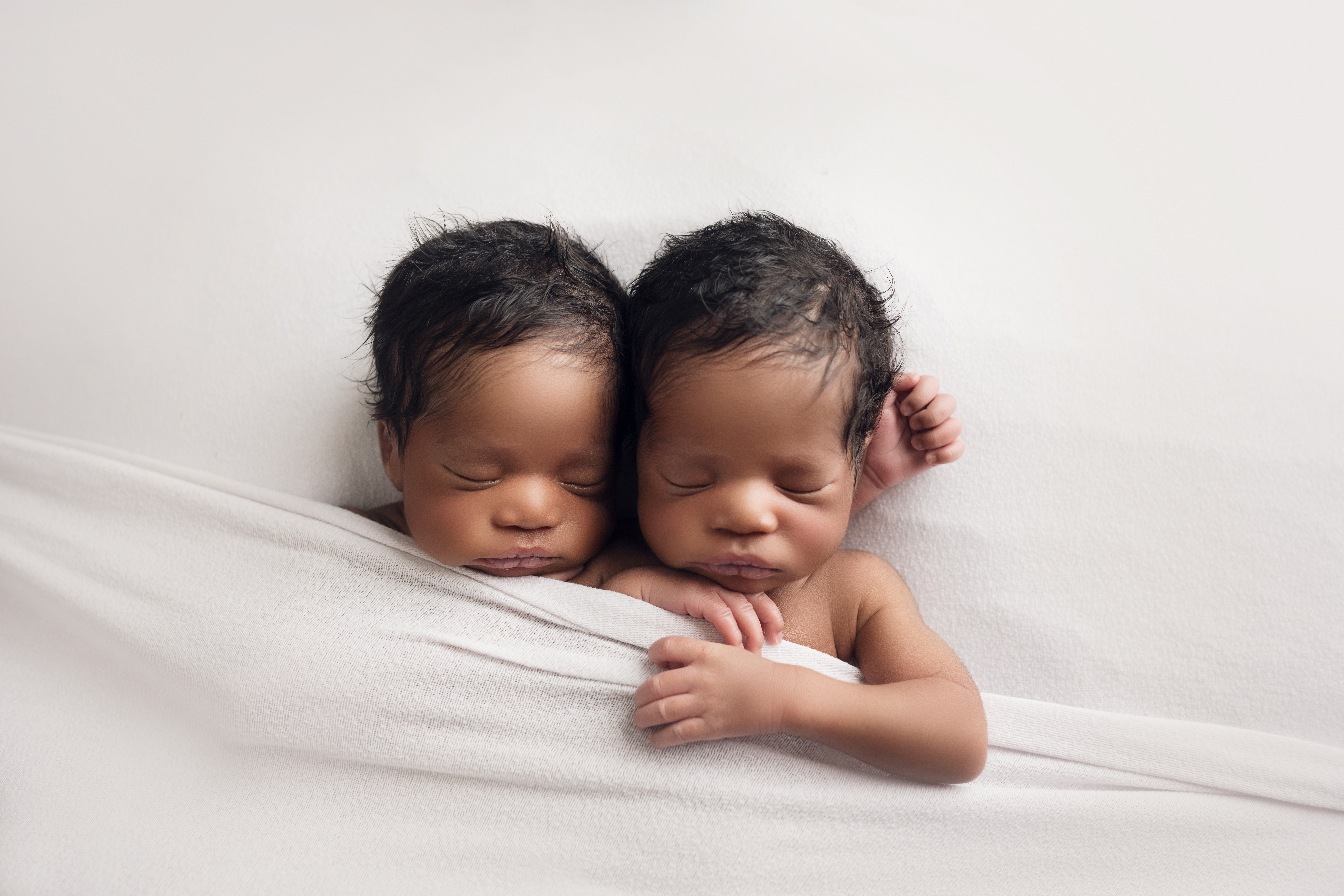 ### Newborn twin boys cuddling together in white blanket