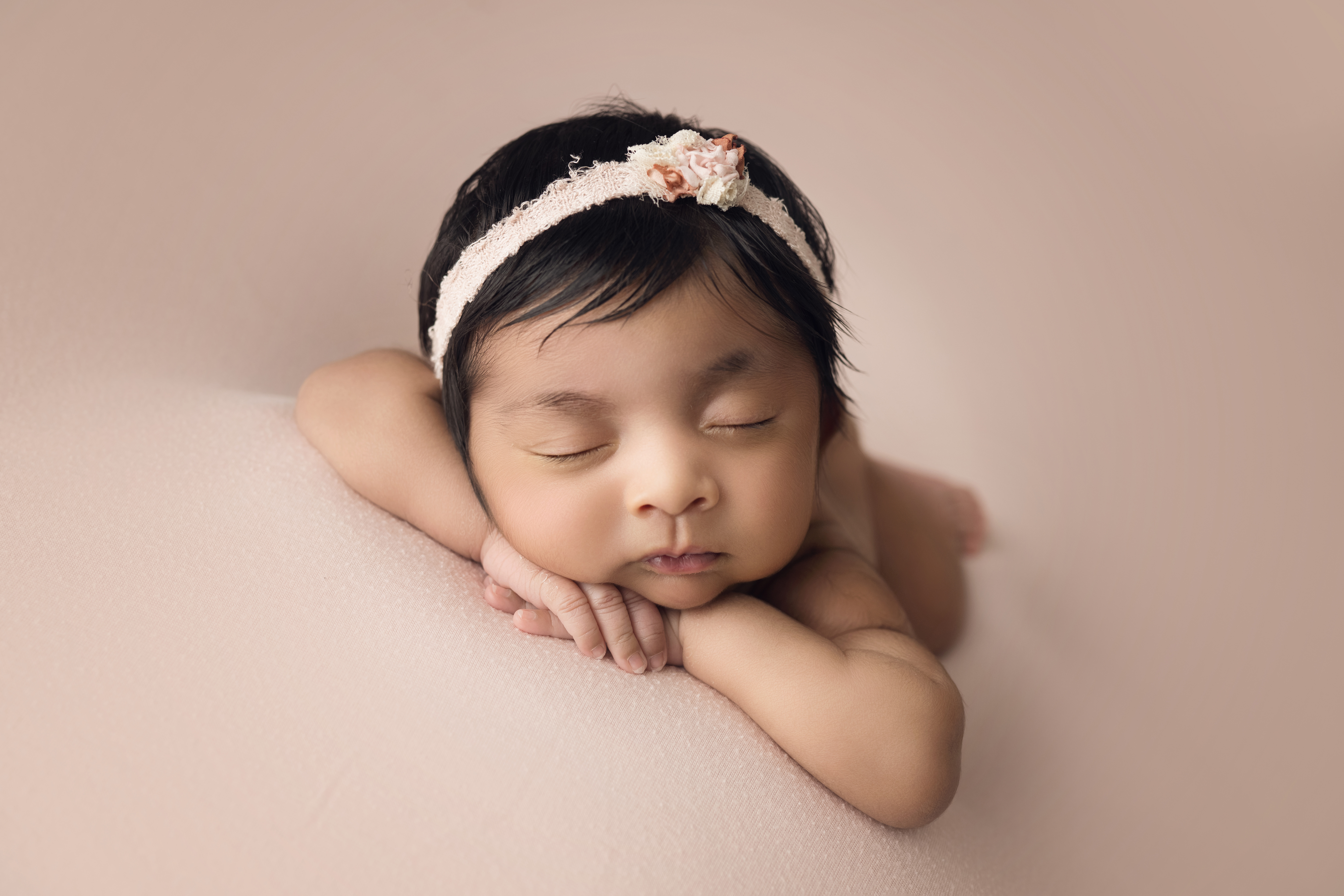 Newborn baby girl on pink blanket with matching bow face forward