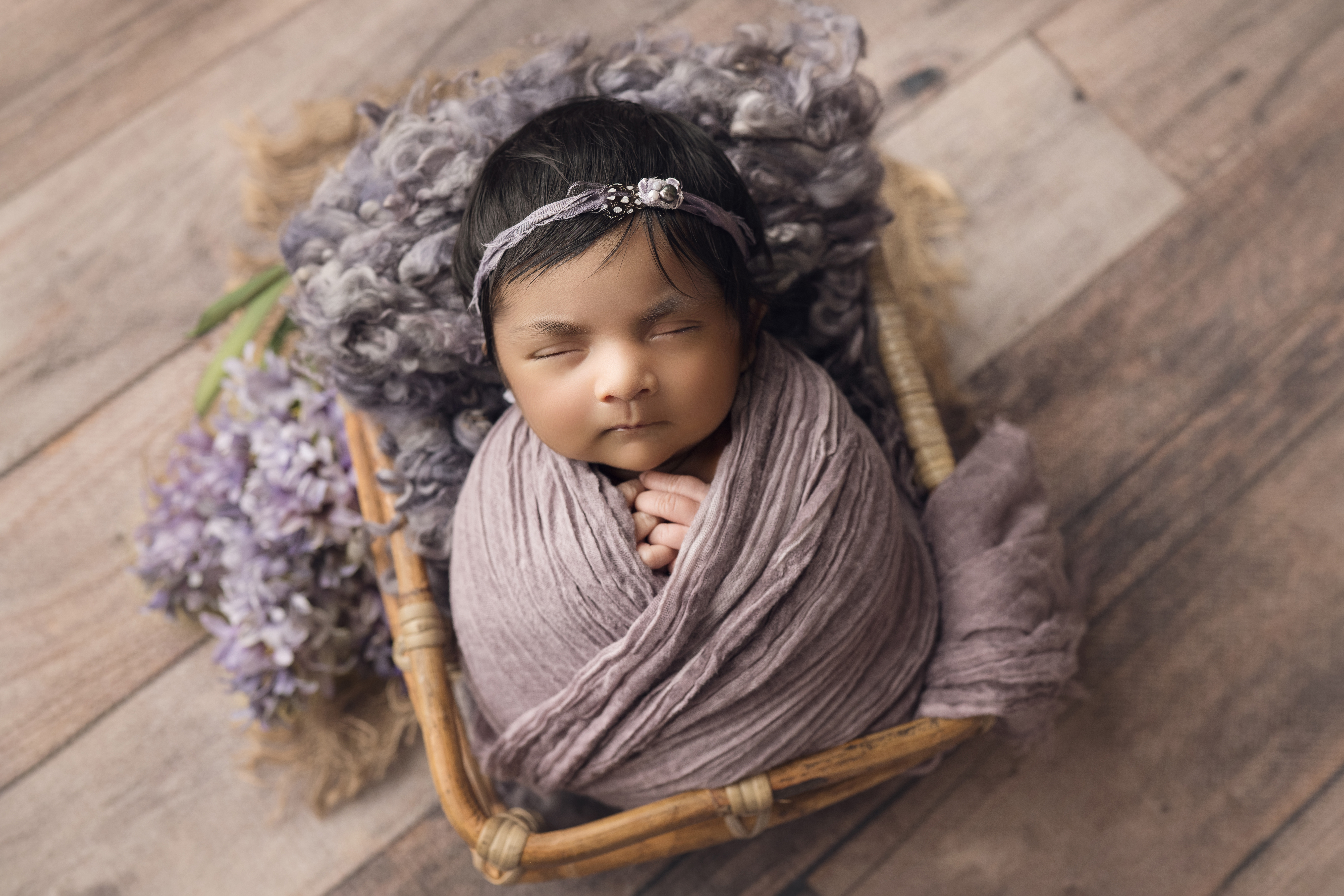 Newborn baby girl wrapped in purple with matching bow in bamboo basket