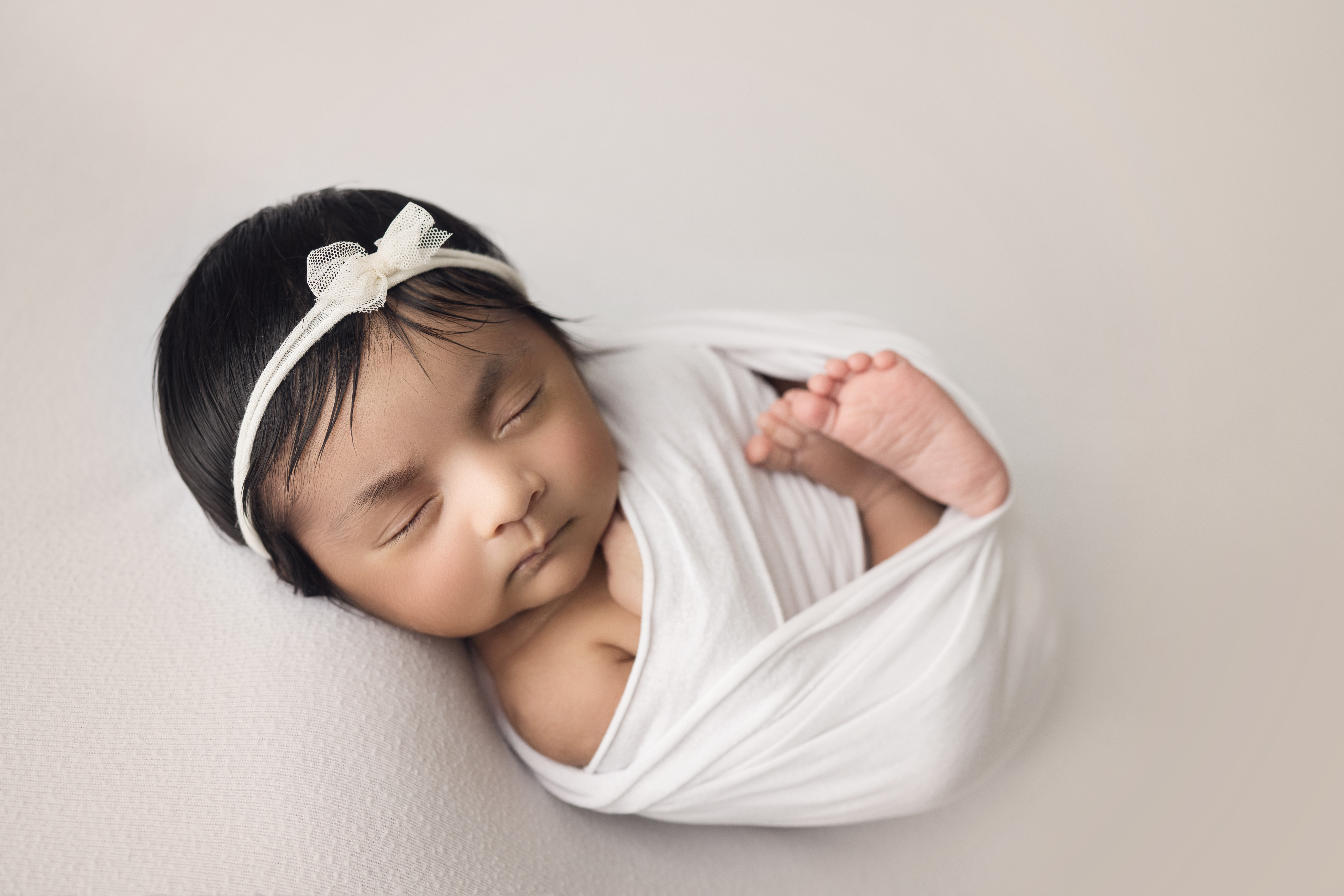 ### Newborn baby girl wrapped in white with matching bow on white blanket