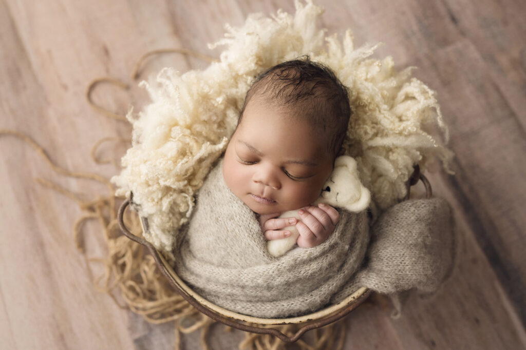 ### Newborn baby boy wrapped in beige holding a teddy bear
