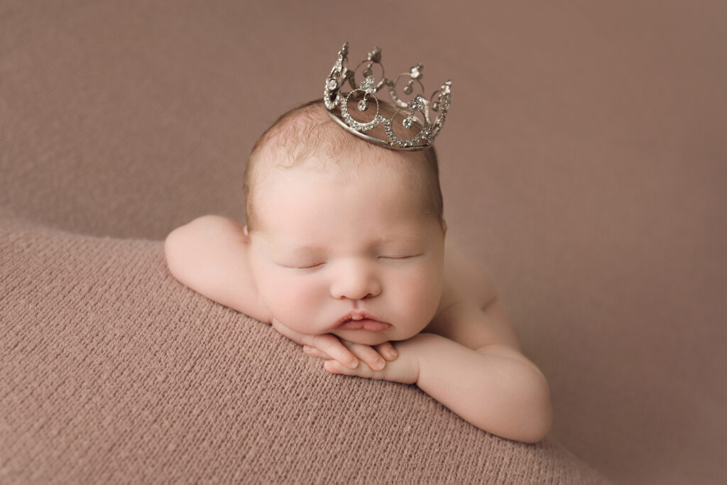 Newborn baby girl on pink blanket face forward wearing crown