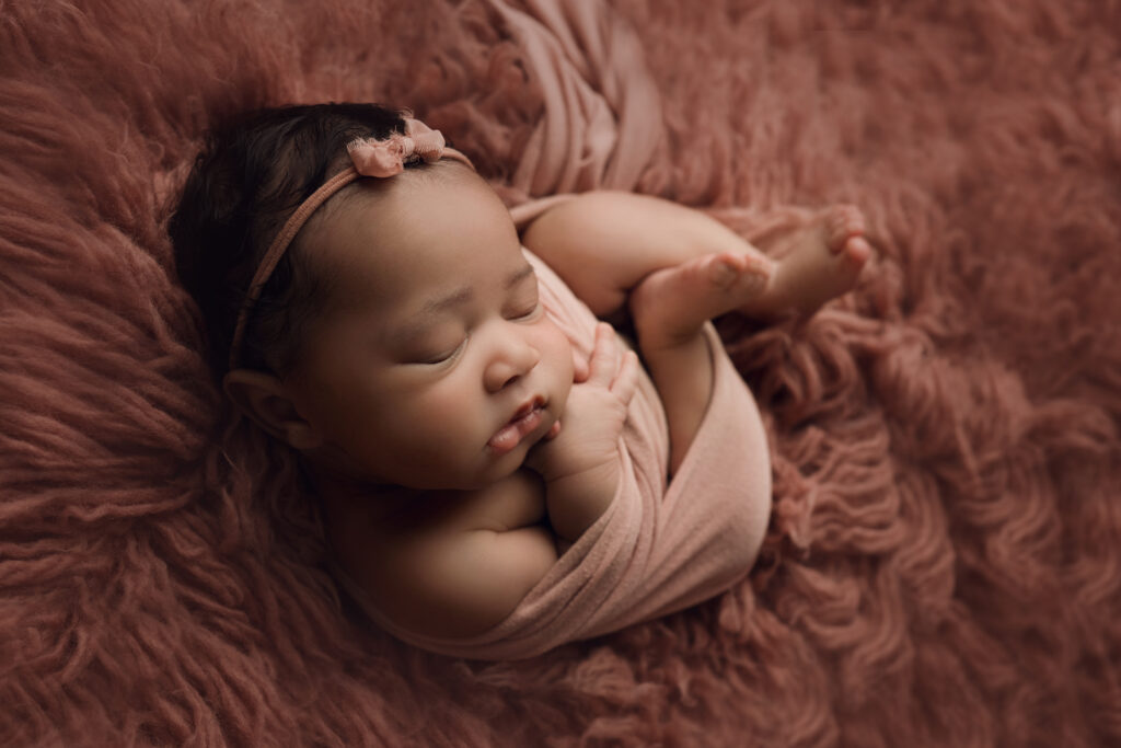 Newborn baby girl curled in pink wrap on pink fur
