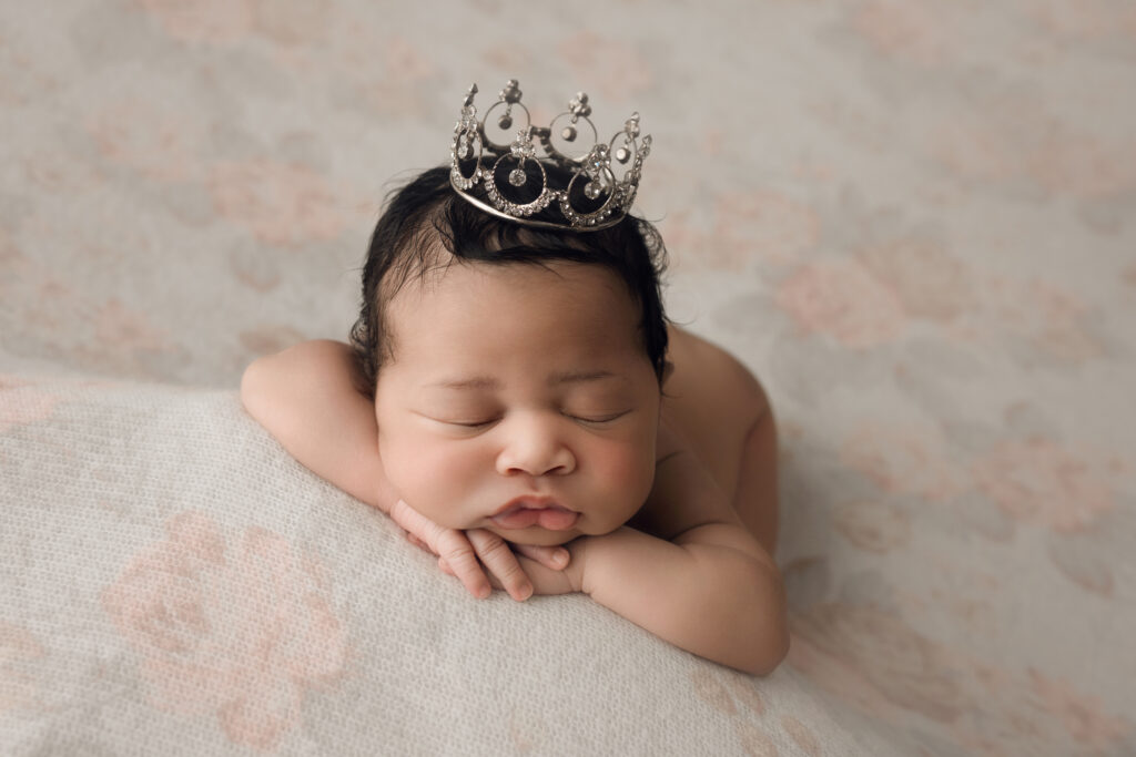 Newborn baby girl face forward on floral blanket with princess crown