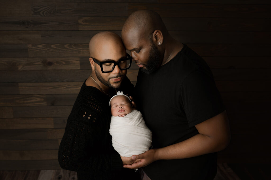 Newborn baby girl with her two dads in cream wrap