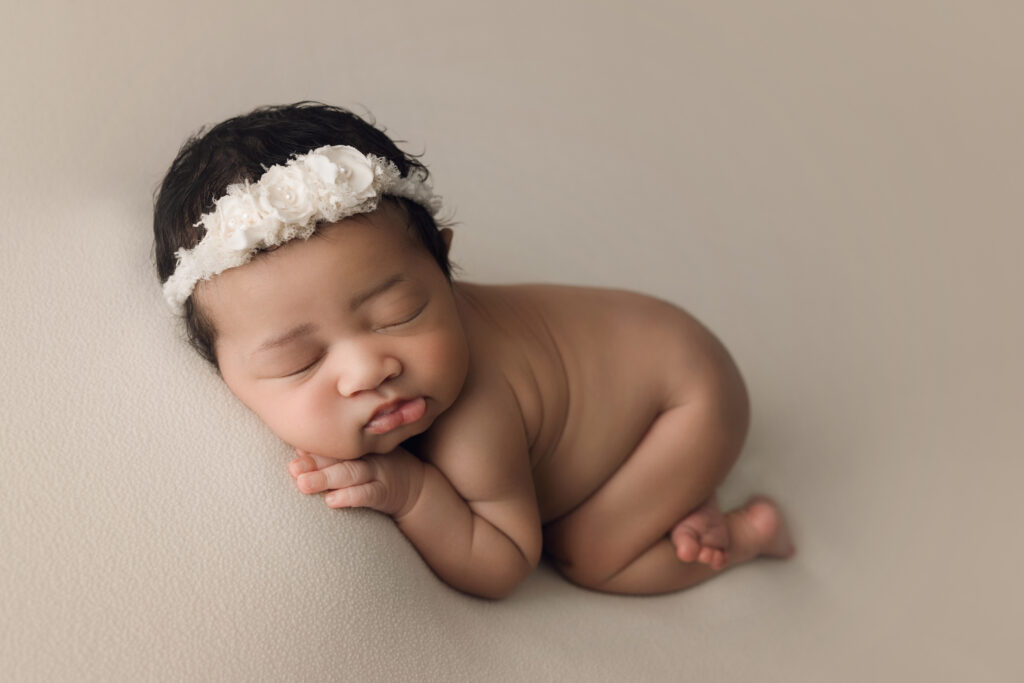 Newborn baby girl with bum up on cream blanket with cream floral headband