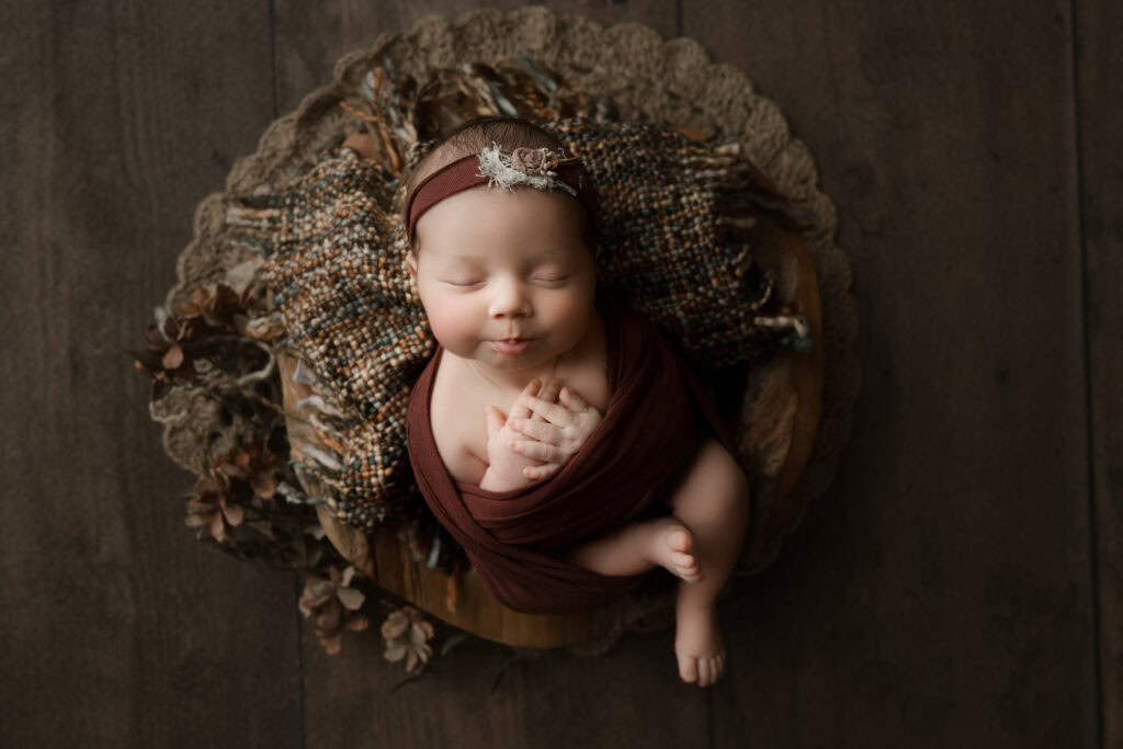 ### Raleigh Newborn Photographer baby girl face up in bowl wrapped in burgandy wrap and matching flowers